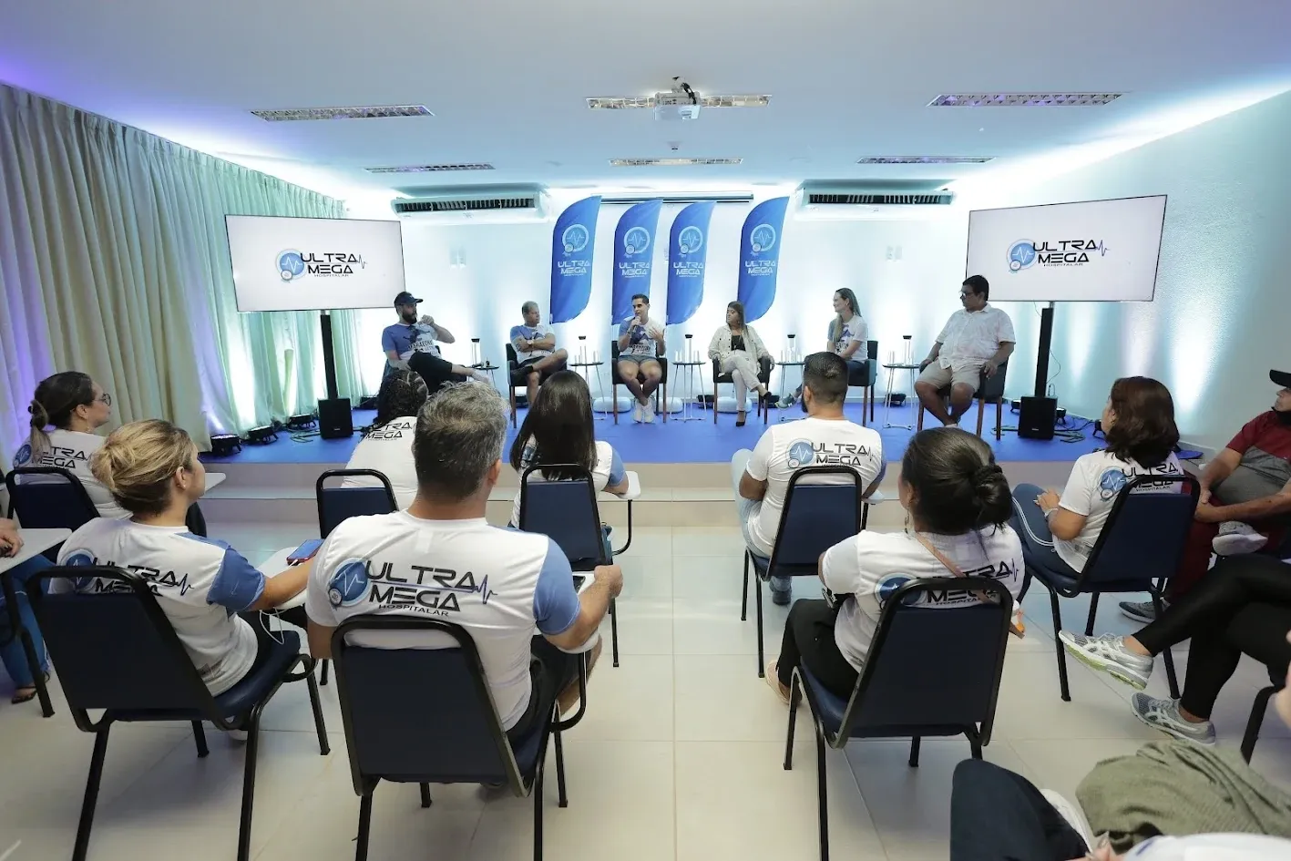 Equipe da Ultramega reunida em um encontro interno, com palestrantes ao fundo