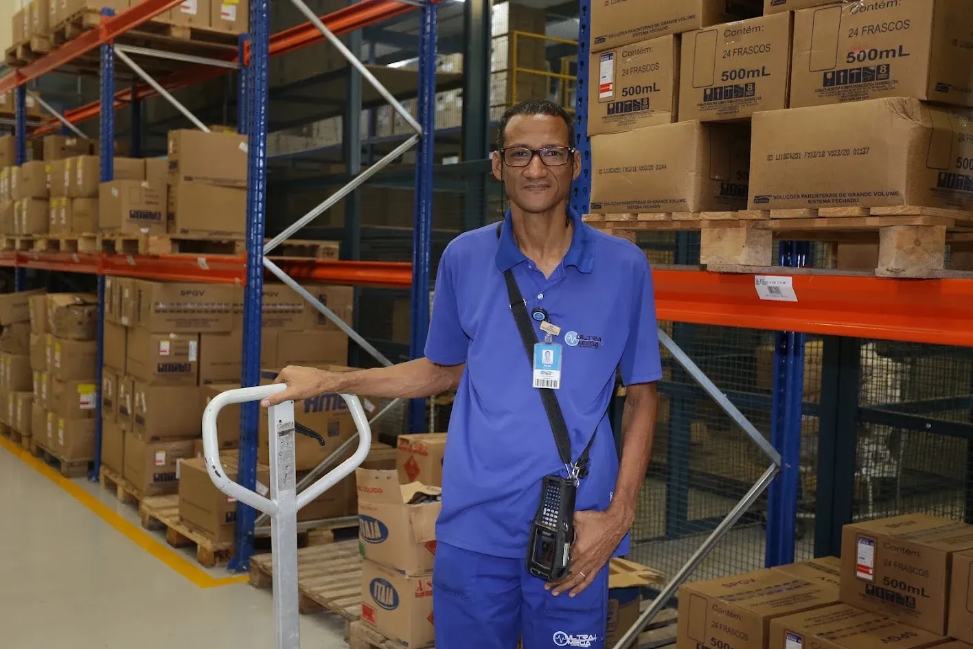 Colaborador da Ultramega no estoque, ao lado de estantes com caixas, sorrindo para a câmera